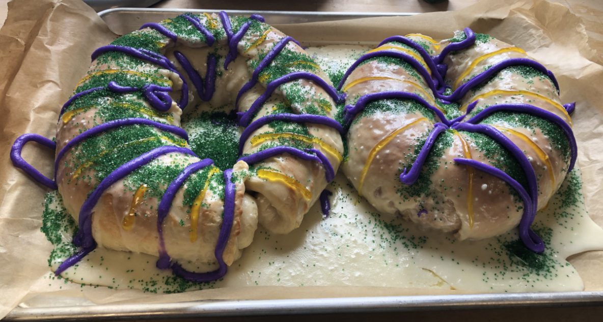 Two loaves of bread, donut-shaped, decorated in purple, yellow and green icing and sprinkles
